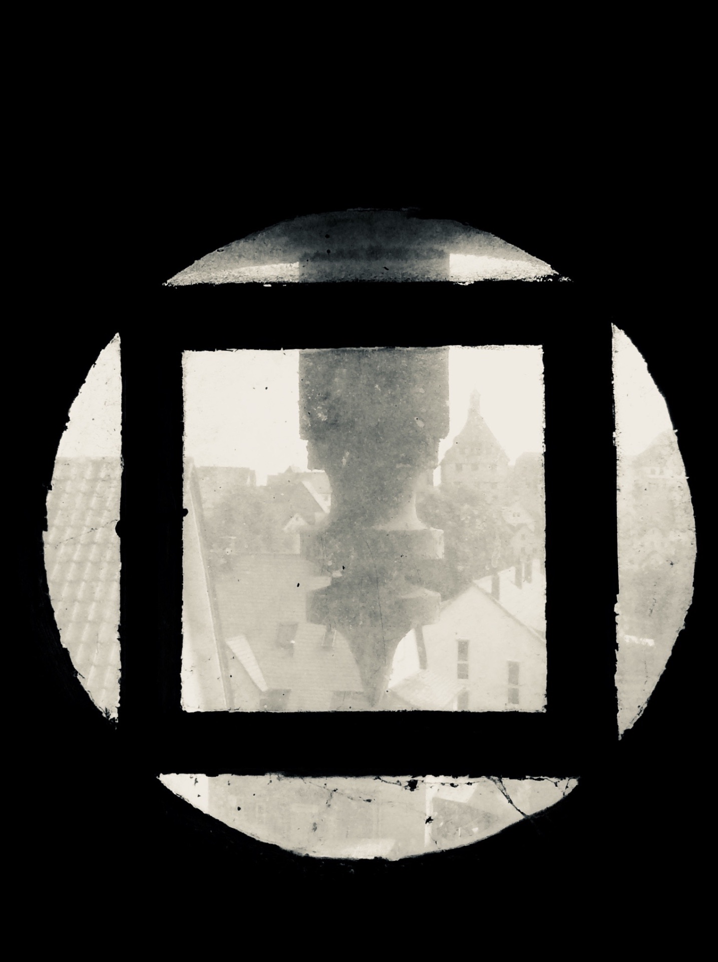 View through a weathered oculus window onto an old town's rooftops